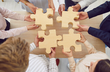 Close up shot of the hands of a business team working to connect wooden puzzles in the office. Teamwork, staff collaboration, and effective work dynamics among the people involved.