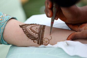 an artist applying intricate henna (mehndi) designs to a person's hand, creating beautiful patterns...