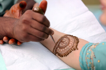 an artist applying intricate henna (mehndi) designs to a person's hand, creating beautiful patterns in a traditional and artistic style. The scene reflects a festive or ceremonial moment.