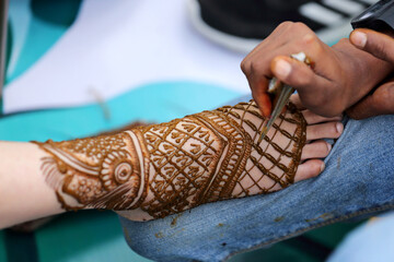 an artist applying intricate henna (mehndi) designs to a person's hand, creating beautiful patterns...