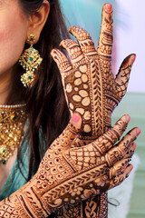 This picture shows a close-up of the intricate bridal mehndi on hands. The bride's gold and emerald jewellery complements the rich mehndi designs, creating a beautiful and elegant look.