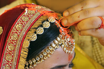 Indian wedding ritual where sindoor (vermilion) is being applied to the bride's hair parting, symbolizing the sacred bond of marriage.