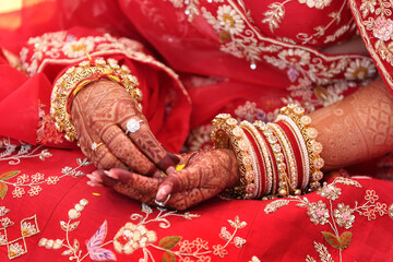 A bride's hands with intricate henna designs, traditional red bangles, gold jewelry. She wears a...