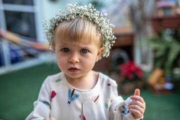 Criança loira com olhos azuis com uma tiara de flores e vestido com estampas