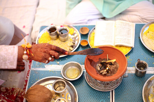 A Hindu ritual with offerings being made into a sacred fire, surrounded by ceremonial items and an open scripture.