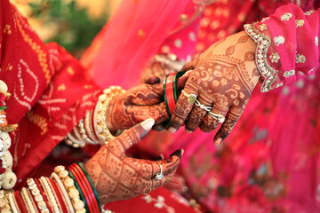 Indian wedding moment, with hands adorned in intricate henna designs, vibrant red bangles, and...