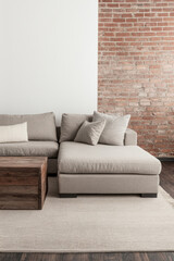 Cozy beige sectional sofa with decorative pillows positioned against a rustic brick wall in a modern living room setting