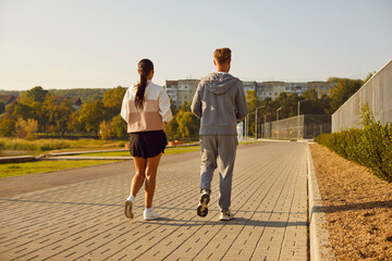 Fototapeta premium Back view of sporty young man and woman wearing sportswear jogging in the park having sport workout for health in nature. Couple running in nature. Jog exercising and healthy lifestyle concept.
