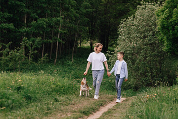 Mother with her son and a beagle dog walk hand in hand in a green park in the summer. Concept of family time, friendship, care