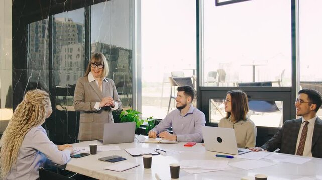 A highly qualified business team participates in a productive meeting led by an elderly gray-haired female director in a modern office space.