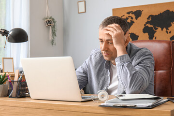 Obraz premium Mature male freelancer working with laptop at table in office