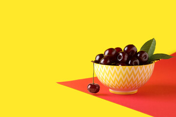 Bowl with sweet cherries and leaves on colorful background