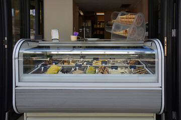 A modern ice cream parlour display case with a variety of colourful ice cream flavours. The case has a curved glass top and a sleek stainless steel base.Ice cream cones dispenser on top of the counter