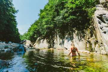 Blonde woman in bikini swimming and relaxing in a clear water river with rock cliffs and free stones. Clarendon Gorge, Vermont, New England, USA.