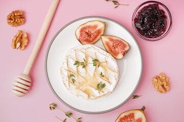 Plate of tasty baked Camembert cheese on pink background
