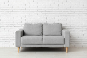 Cozy grey sofa near white brick wall