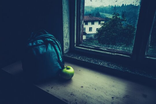 Rainy day still life: apple and backpack by an old window overlooking countryside - Powered by Adobe