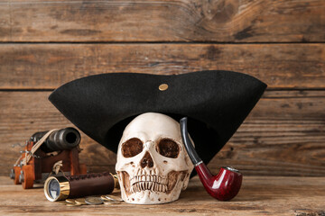 Human skull with pirate hat, spyglass and smoking pipe on brown wooden background