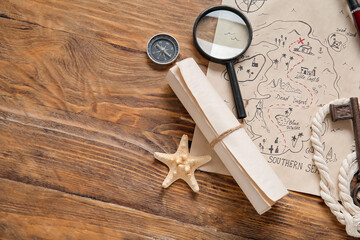 Treasure map with magnifier, scroll and compass on brown wooden background