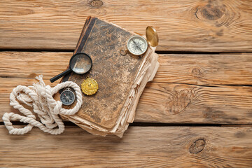 Old manuscripts with compasses, magnifier and golden pirate amulet on brown wooden background