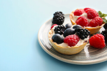 Plate of tasty tartlets with whipped cream and berries on blue background