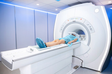 the patient lies on the table during an MRI examination of her body. A large bright room with modern equipment and blue lighting. bare legs and clothes covered with a sterile gown. shoe covers