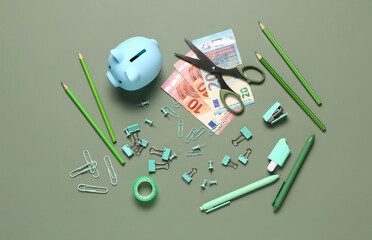 Different school stationery, piggy bank and money on green background