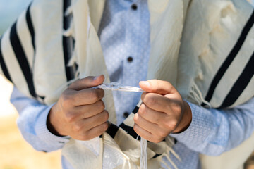 Close-up of a man's hands holding the front tzitzit of his tallit during Shacharit prayer