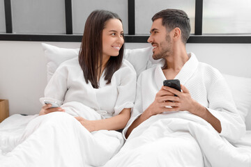Obraz premium Happy young couple with mobile phones lying on bed