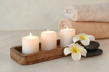 Wooden board with burning candles, spa stones, flowers and clean towels on light background