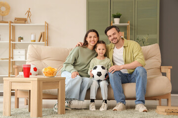 Happy family with soccer ball watching football game at home