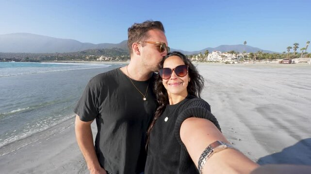happy latin heterosexual couple in love filming in selfie mode on the beach, enjoying the beach	