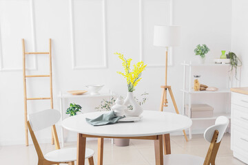 Vase with mimosa flowers on dining table in light kitchen