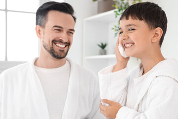 Happy father and his little son applying shaving foam on faces in bathroom