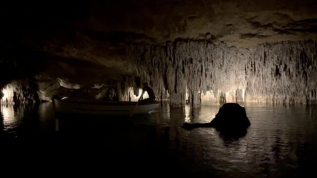 Background. Inside a huge cave. A boat with a helmsman floats along the surface of an underground lake, casting a long shadow on the picturesque stalactites above the water.
