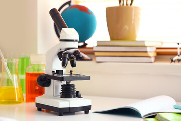 Modern microscope, chemical flasks and copybook on table in teenager's room