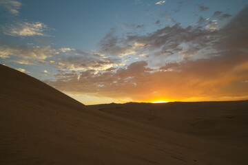 Breathtaking sunset over the sand dunes of Huacachina, Peru, illuminating the sky with vibrant colors and shadows