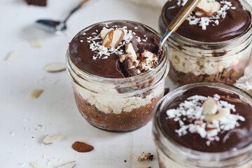 Three jars of homemade chocolate overnight oatmeal with shredded coconut and sliced almonds. Selective focus with blurred foreground and background. A joy to eat for breakfast or snack.