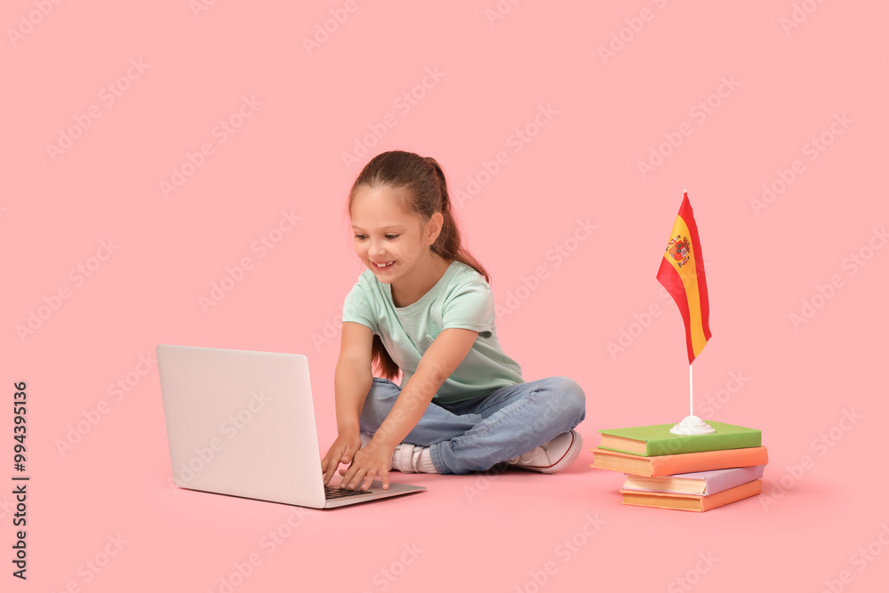 Wall mural Little girl with laptop, books and Spanish flag on pink background