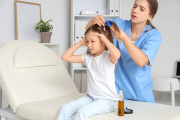 Obraz premium Female doctor combing little girl's hair with pediculosis in clinic