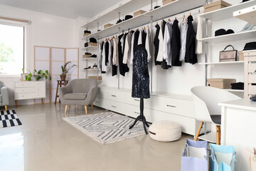 Interior of boutique with stylish clothes, mannequin and armchair