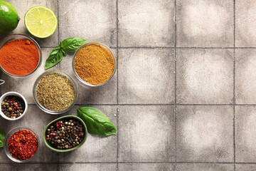 Composition with bowls of different spices, basil and lime on grunge tile background