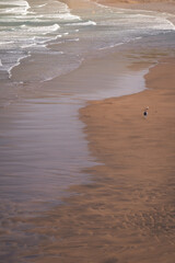 wave on a infinity beach with a person walking in the sand and water 