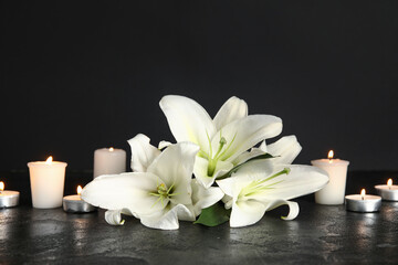 Beautiful white lily flowers and burning candles on dark table