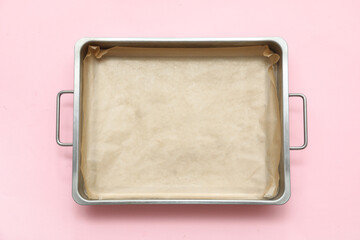 Metal baking tray with parchment paper on pink background