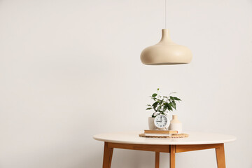 Alarm clock with books on table and pendant lamp near light wall