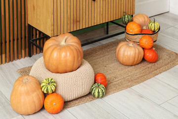 Wicker basket of different pumpkins near wooden commode at home