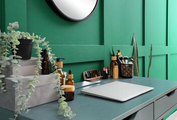 Laptop with makeup products and plant on table in room