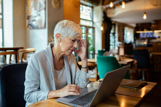 Senior businesswoman working on laptop in a cafe with wireless earbuds