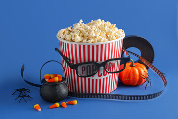 Bucket of tasty popcorn, 3D glasses, candy corns and decor for Halloween on color background
